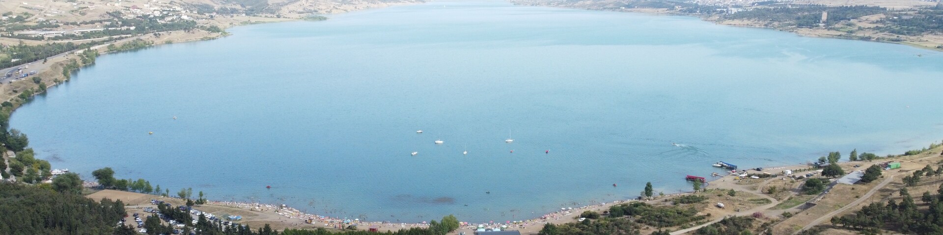 A large lake surrounded by hills and a small town with visible buildings and parked cars.