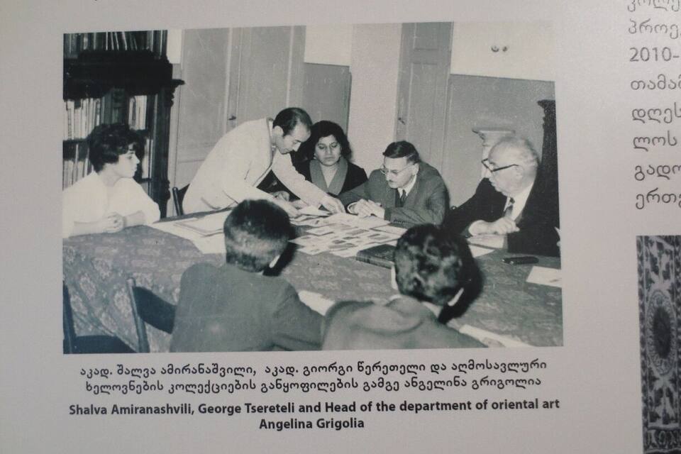 A group of people around a table with papers, in a room with bookshelves.