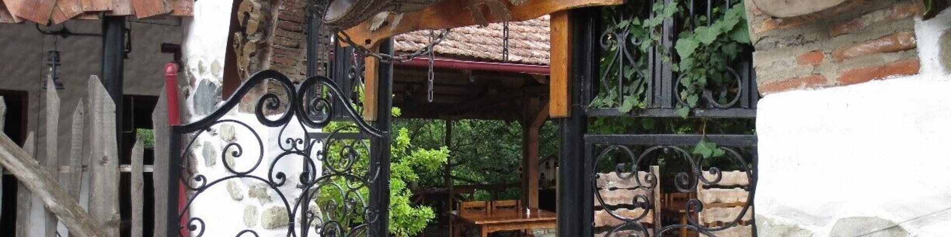 A rustic outdoor seating area with a wrought iron gate, wooden furniture, and a stone wall.