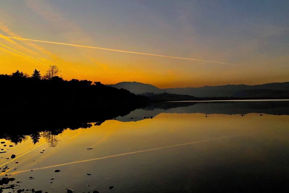 Un lago tranquilo al atardecer, con un reflejo claro del cielo y montañas distantes.