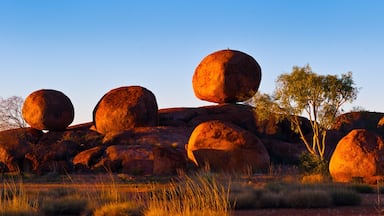 A landscape with large red rock formations and sparse vegetation under a clear sky.