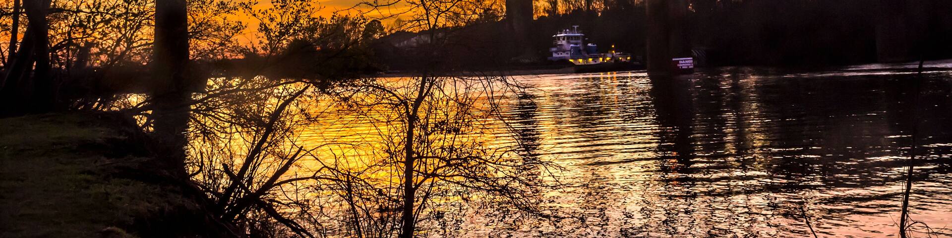 A steel bridge over a river at sunset with a reflection of the sky.