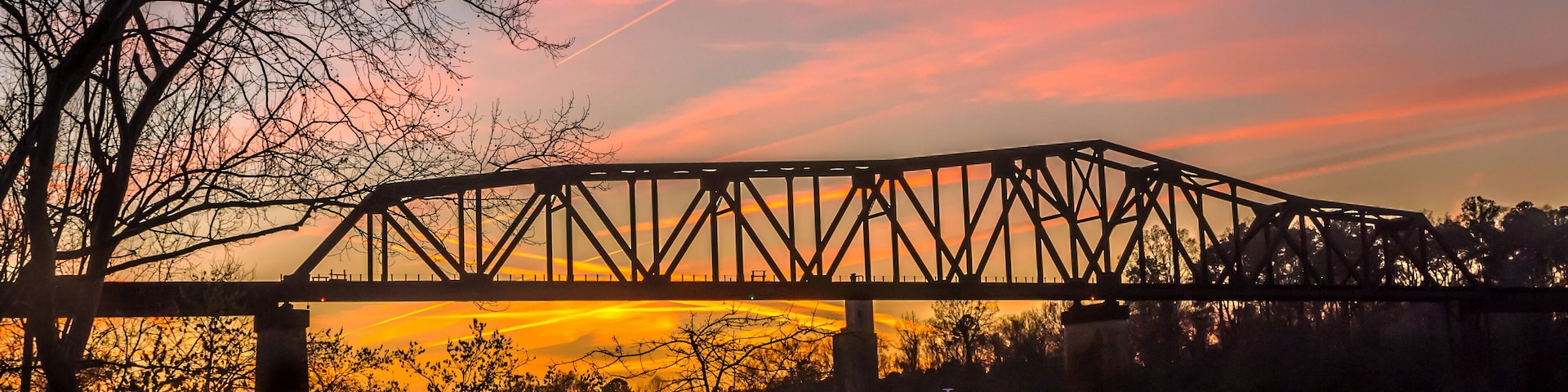 Uma ponte de aço sobre um rio ao pôr do sol, refletindo o céu.