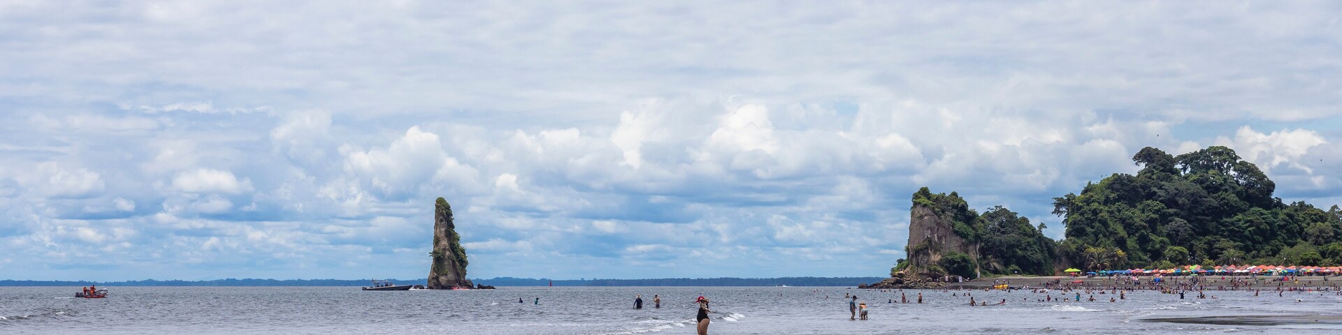 Una playa con una roca destacada, una orilla arenosa y una zona boscosa en la distancia.
