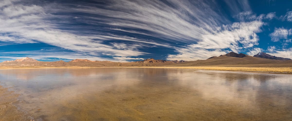 A desert landscape with a clear sky, a reflective body of water, and distant mountains.