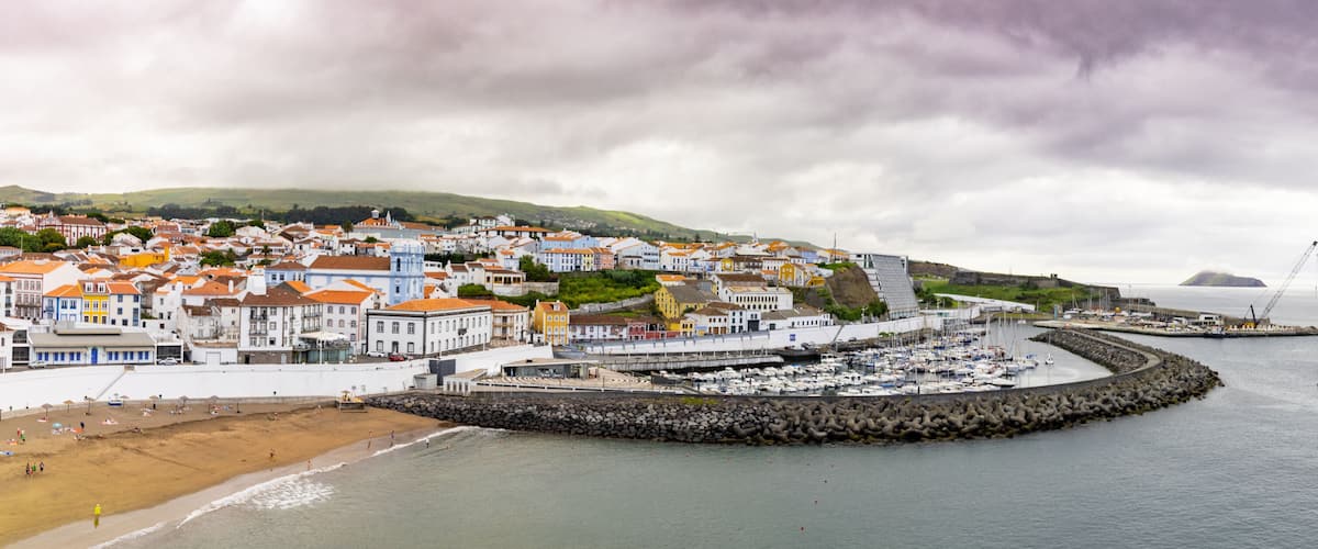 A coastal town with colorful buildings, a rocky breakwater, and boats in the harbor.