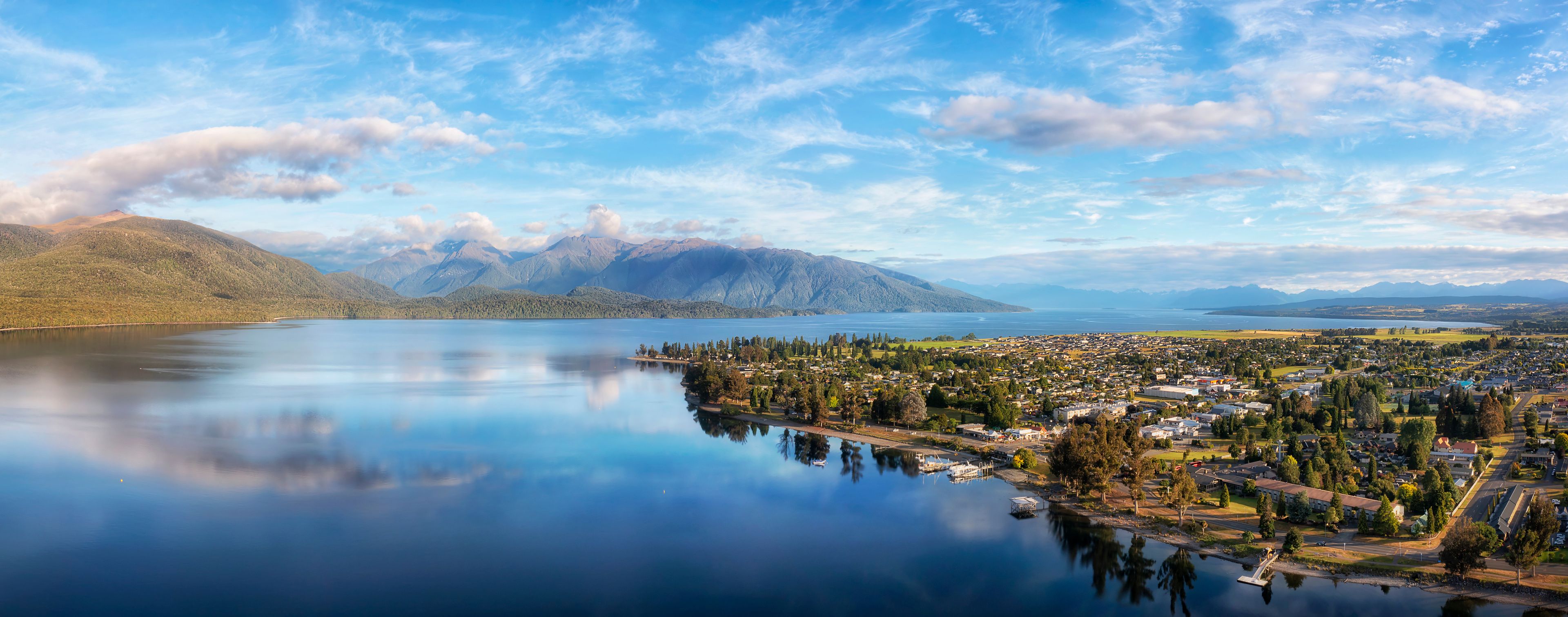 A lake with mountains in the background, a town in the foreground, and a clear sky.