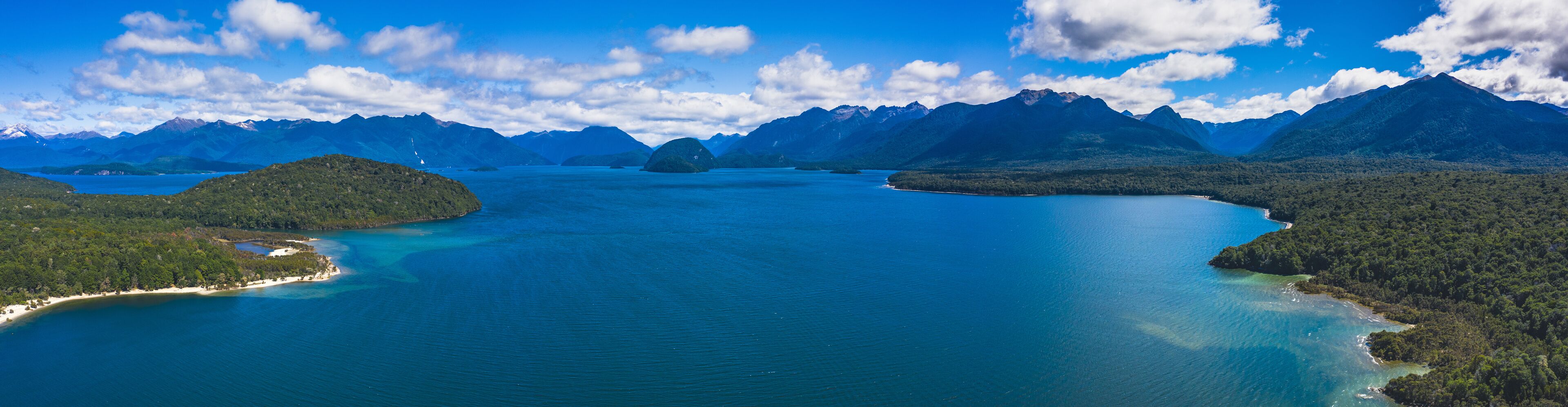 A large body of water surrounded by mountains and forested areas.