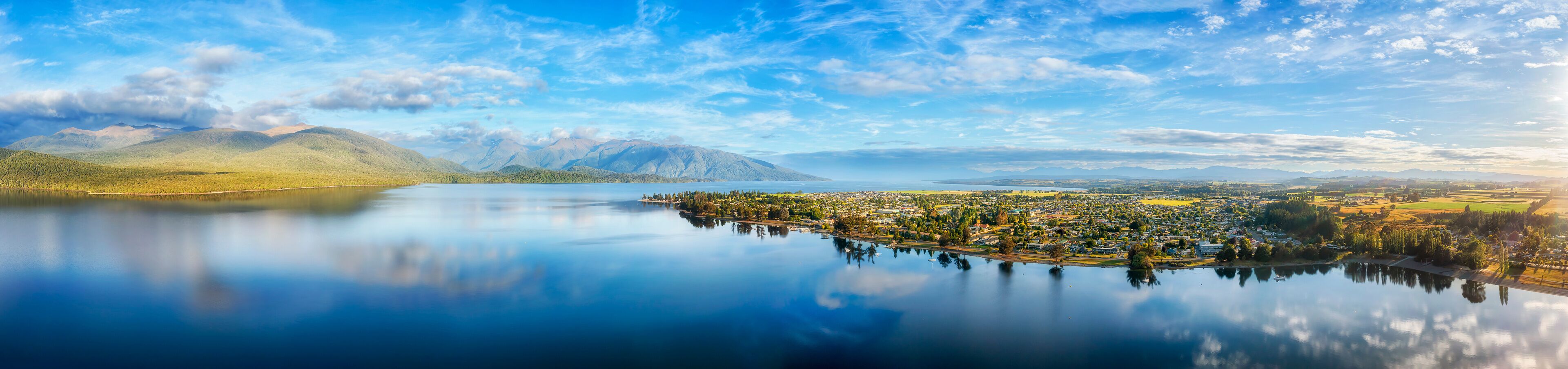 A calm lake with a town in the foreground and mountains in the background.