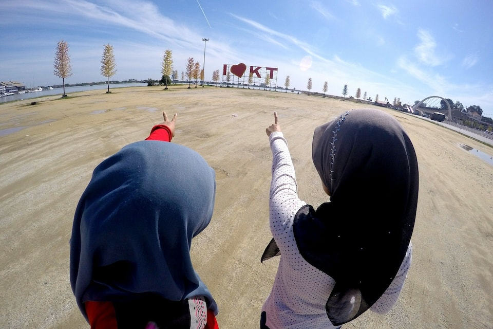 Two people pointing towards a large sign with the letters "KT" and a heart symbol.