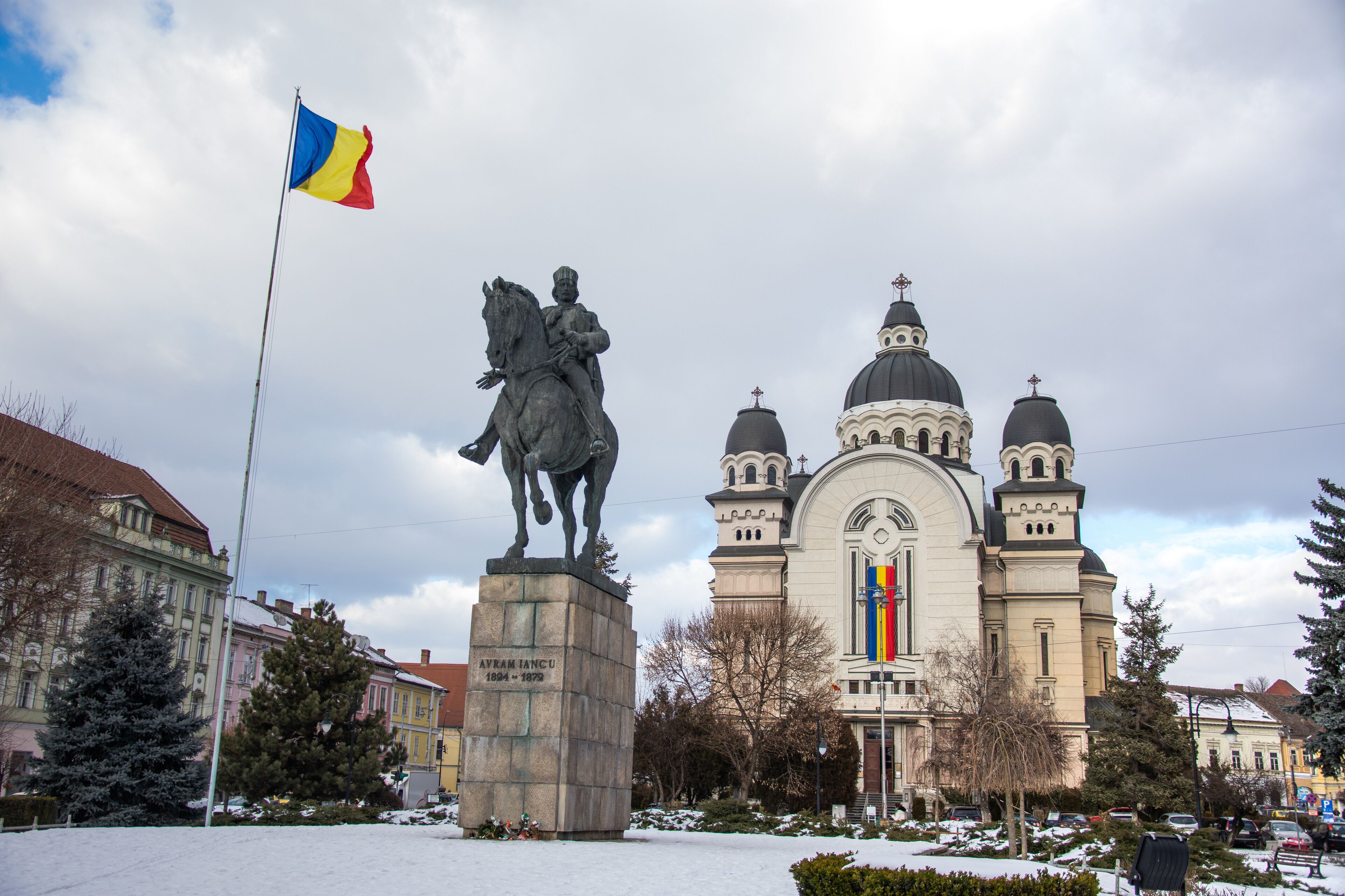 A statue of a man on a horse, a church with domes, and a flag.