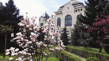 Un edificio de estilo arquitectónico tradicional, rodeado de setos cuidados y árboles en flor.