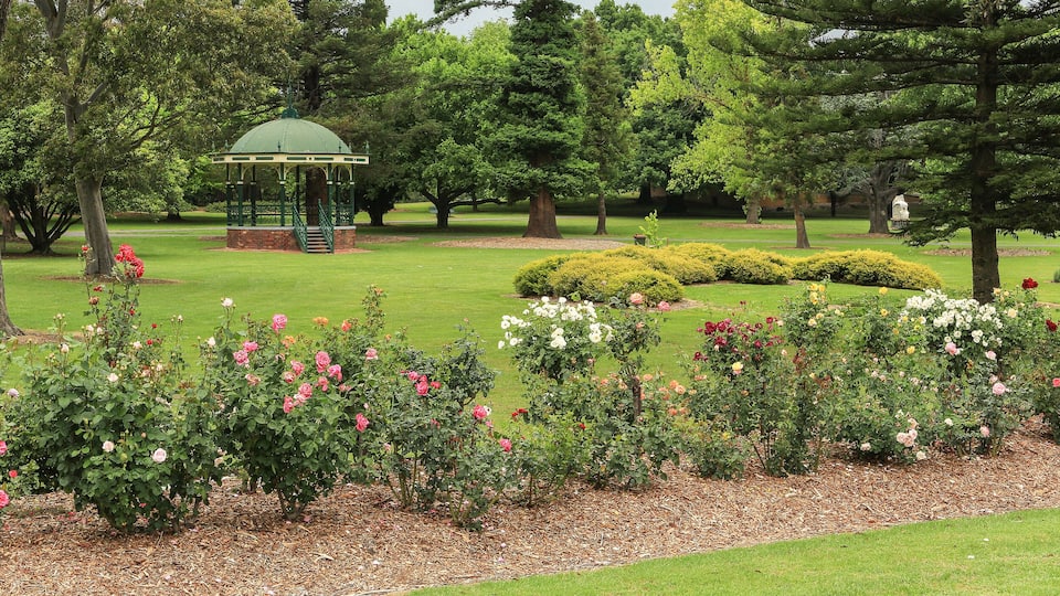 A park with a gazebo, rose bushes, and a well-maintained lawn.