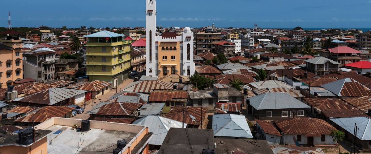 A coastal cityscape with a prominent white church tower, colorful buildings, and a mix of residential and commercial structures.