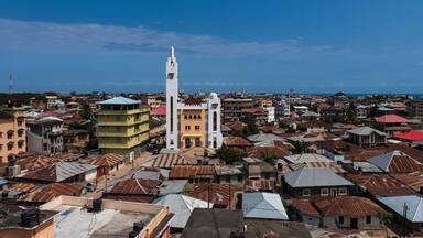 Un paisaje urbano costero con una imponente torre de iglesia blanca, edificios de colores y una mezcla de construcciones residenciales y comerciales.