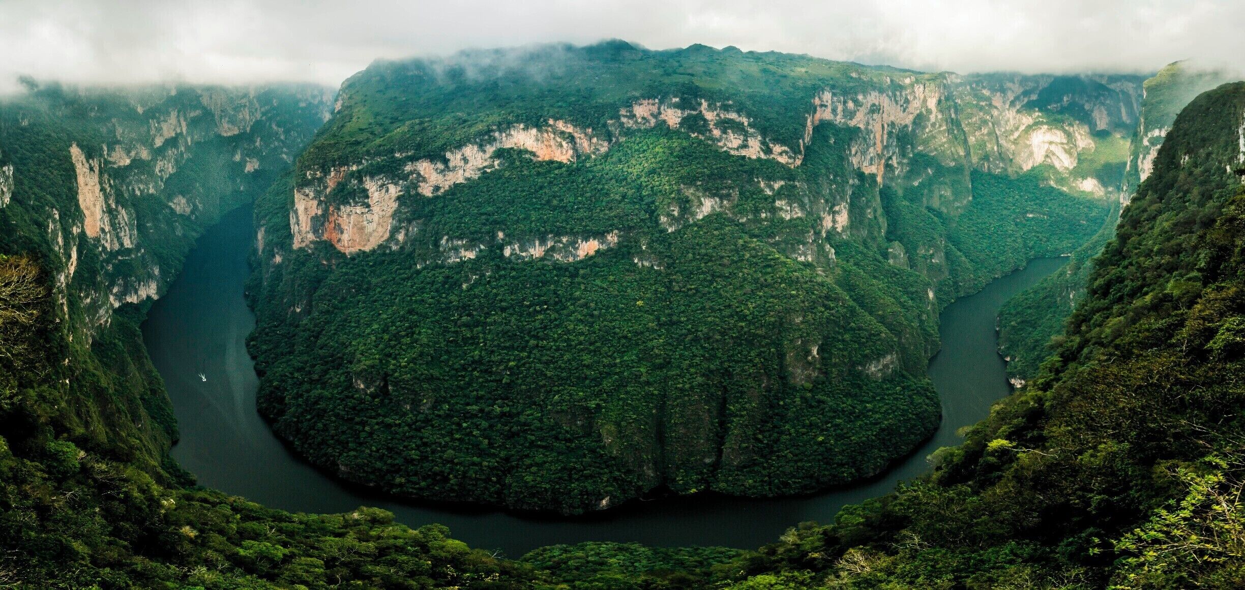 A deep valley with steep cliffs and dense green forest.