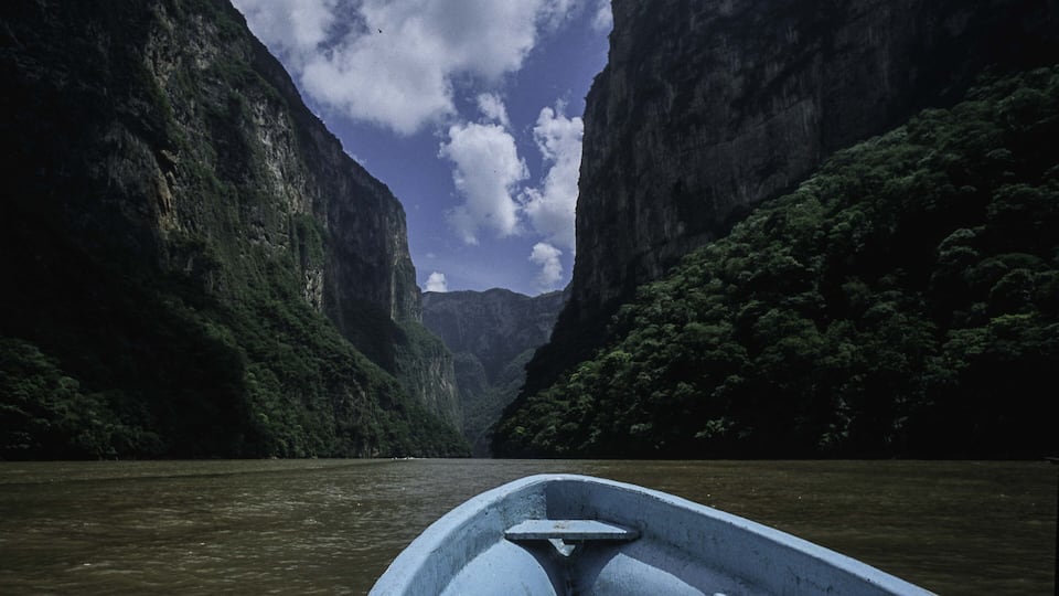 A narrow river canyon with steep cliffs and dense greenery on both sides.