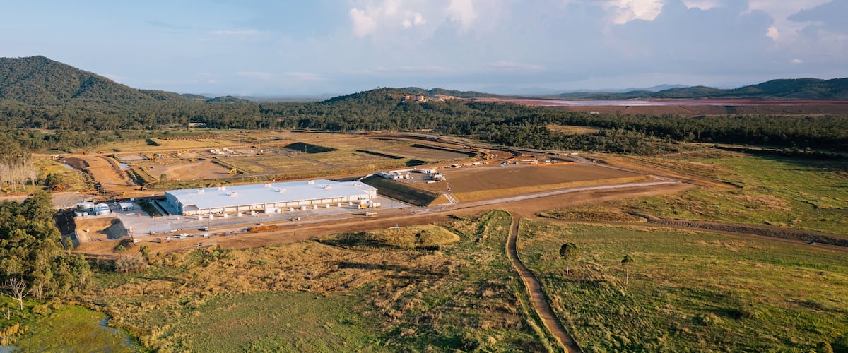 An industrial facility surrounded by forested hills and open fields.