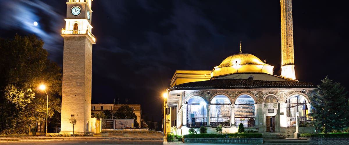 A mosque with a minaret and a clock tower at night.