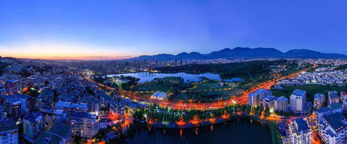 Panoramic aerial image of the city of Tirana from the outer ring road showing the artificial lake after the Sunset.