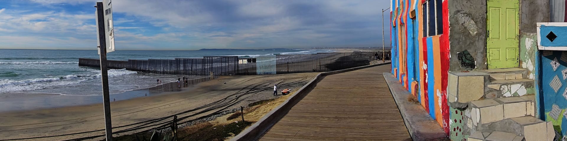A coastal walkway with a wooden boardwalk, colorful buildings, and the ocean in the background.