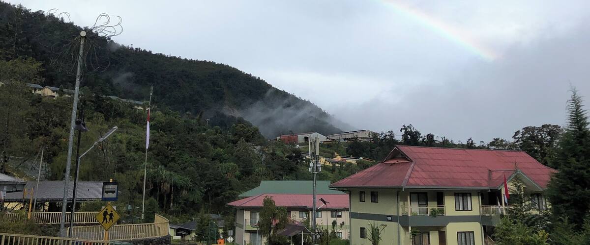 A rural landscape with a rainbow, houses, and a hill in the background.