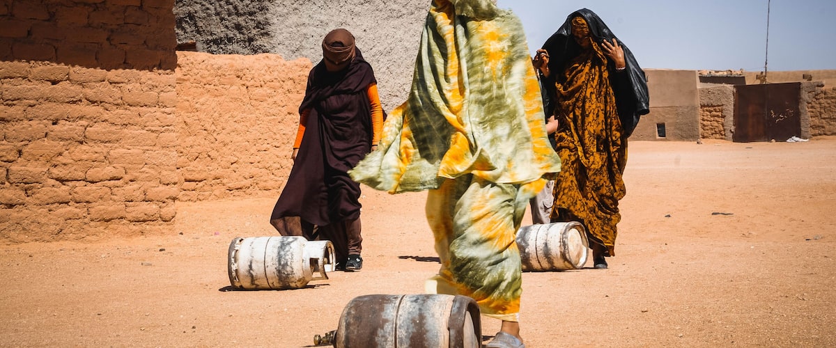 A desert landscape with people carrying barrels.