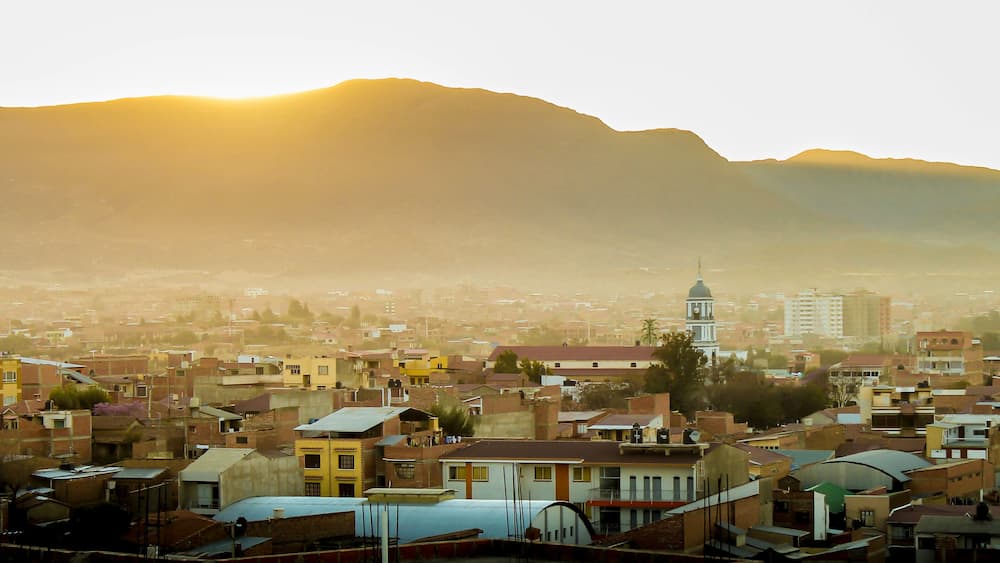 A cityscape with a prominent clock tower and mountains in the background.