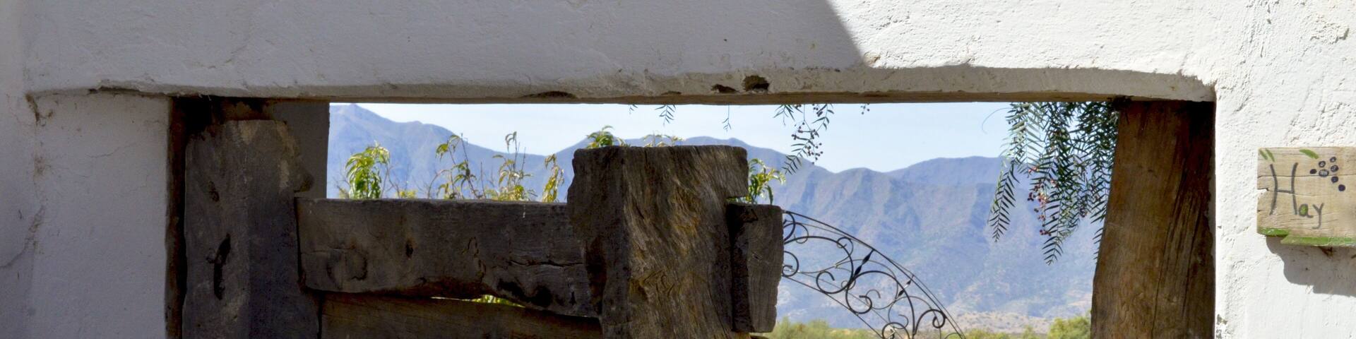 A rustic wooden gate with a sign reading "Hay" in a rural setting with mountains in the background.