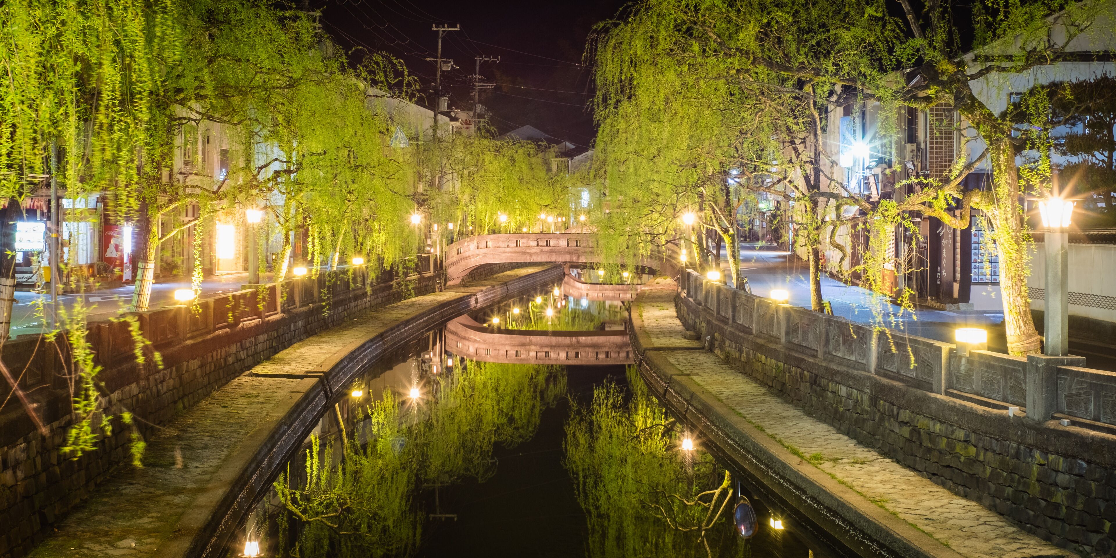 Un canal nocturno con muros de piedra y árboles que reflejan luces.
