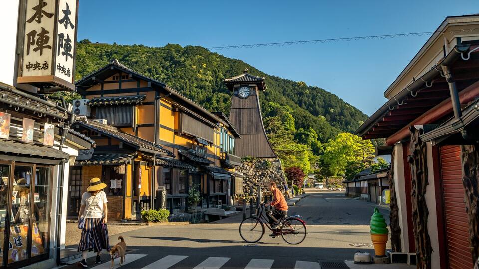 A traditional Japanese street with buildings, a clock tower, and a person riding a bicycle.