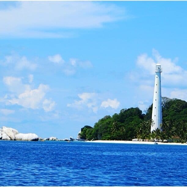 A white lighthouse on a small island with clear blue water and white sand.