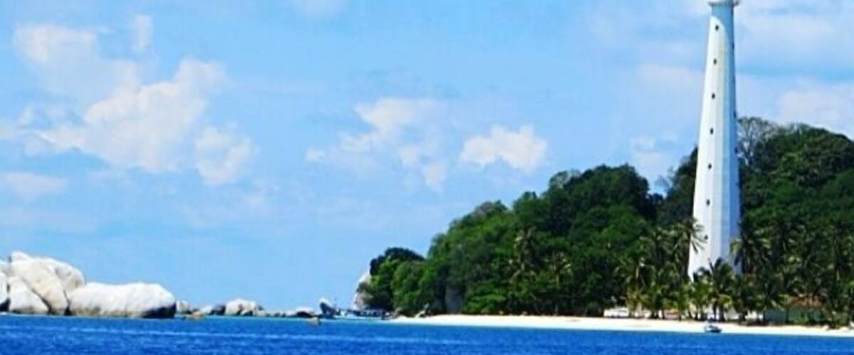 A white lighthouse on a small island with clear blue water and white sand.