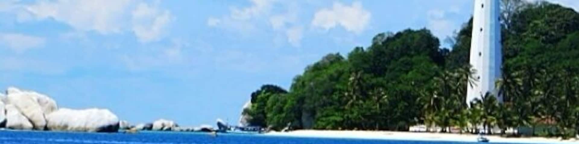 A white lighthouse on a small island with clear blue water and white sand.