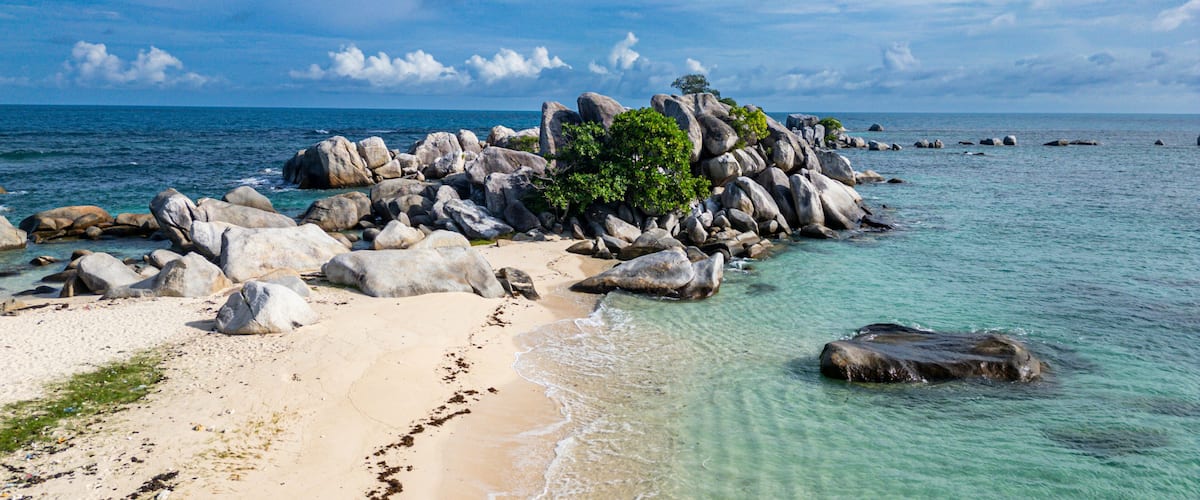 A beach with clear turquoise water, large rocks, and a small island with greenery.