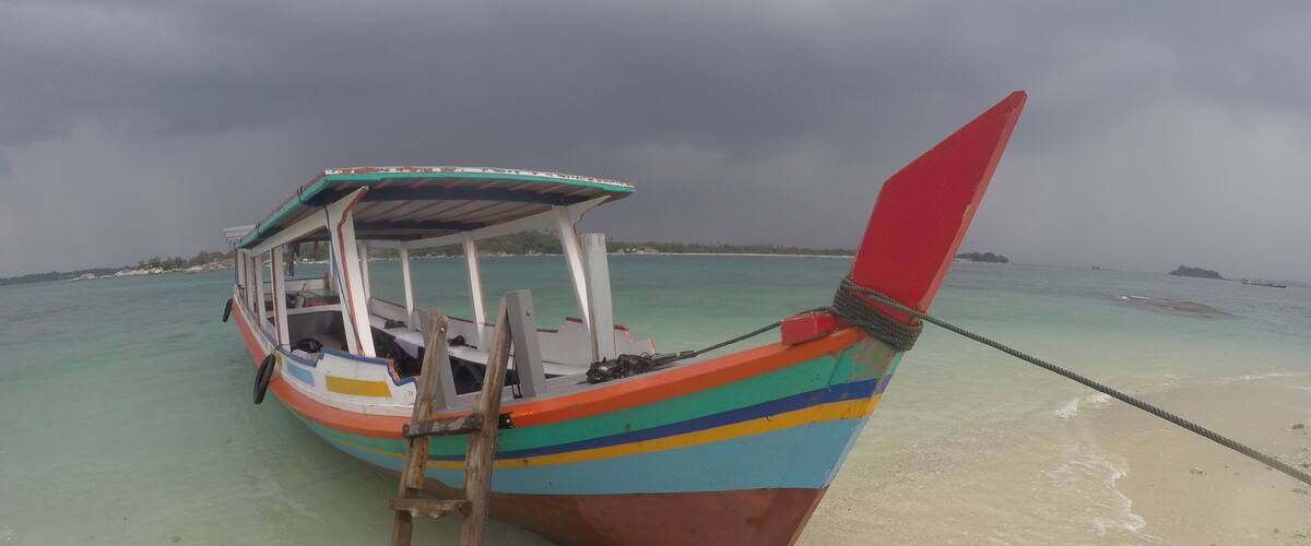 A colorful boat with a ladder, tied to a sandy beach with clear turquoise water.
