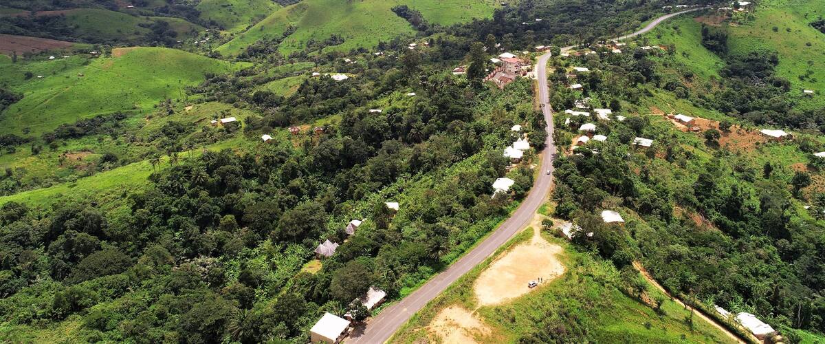 A valley with a winding road, green hills, scattered houses, and dense vegetation.