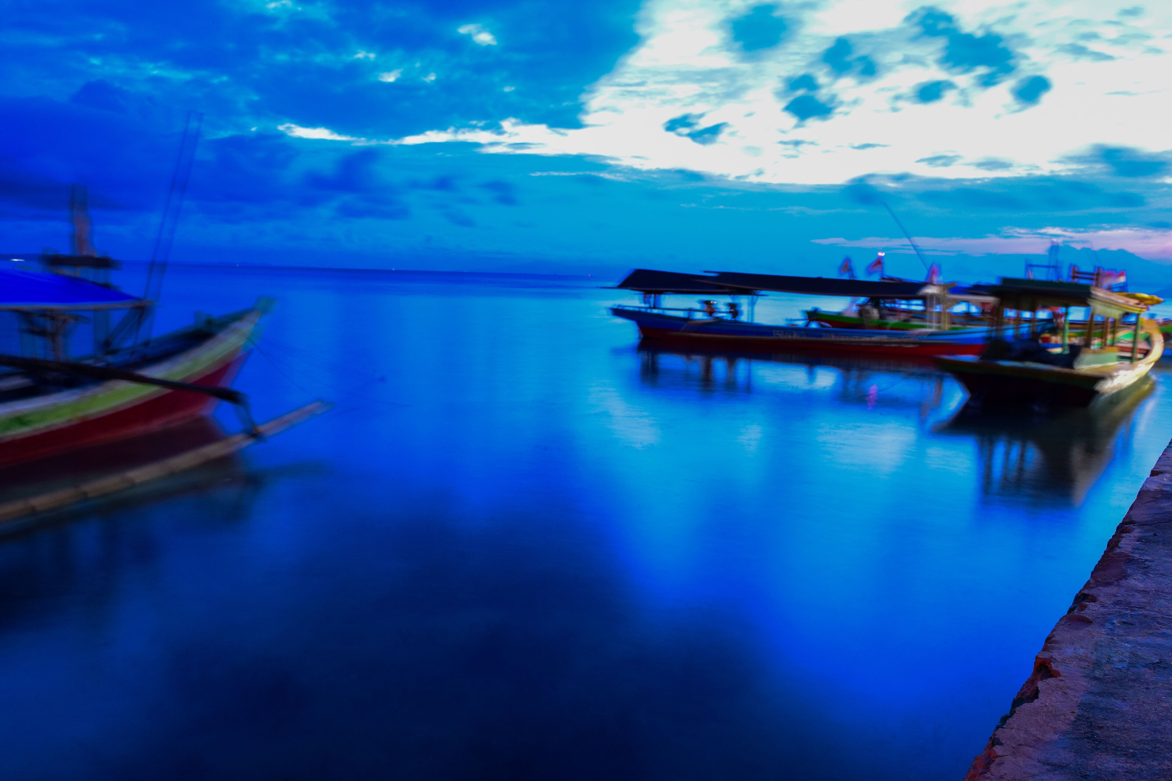 A calm body of water with boats docked along the shore.