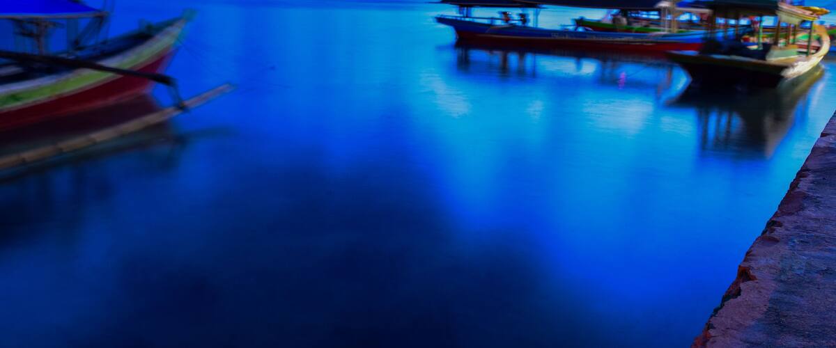 A calm body of water with boats docked along the shore.