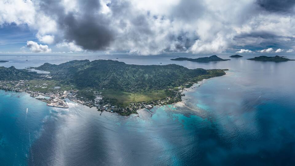 An island with a runway, surrounded by turquoise waters and a cloudy sky.