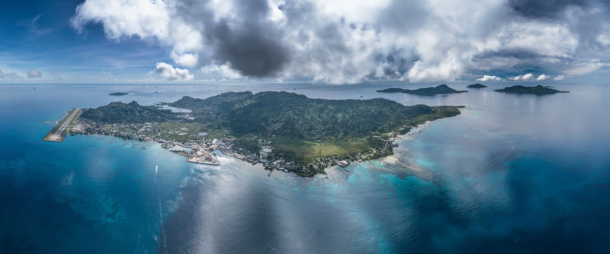 An island with a runway, surrounded by turquoise waters and a cloudy sky.
