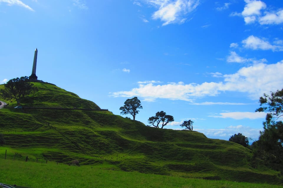 Uma colina verde com um monumento alto no topo e um céu azul límpido.
