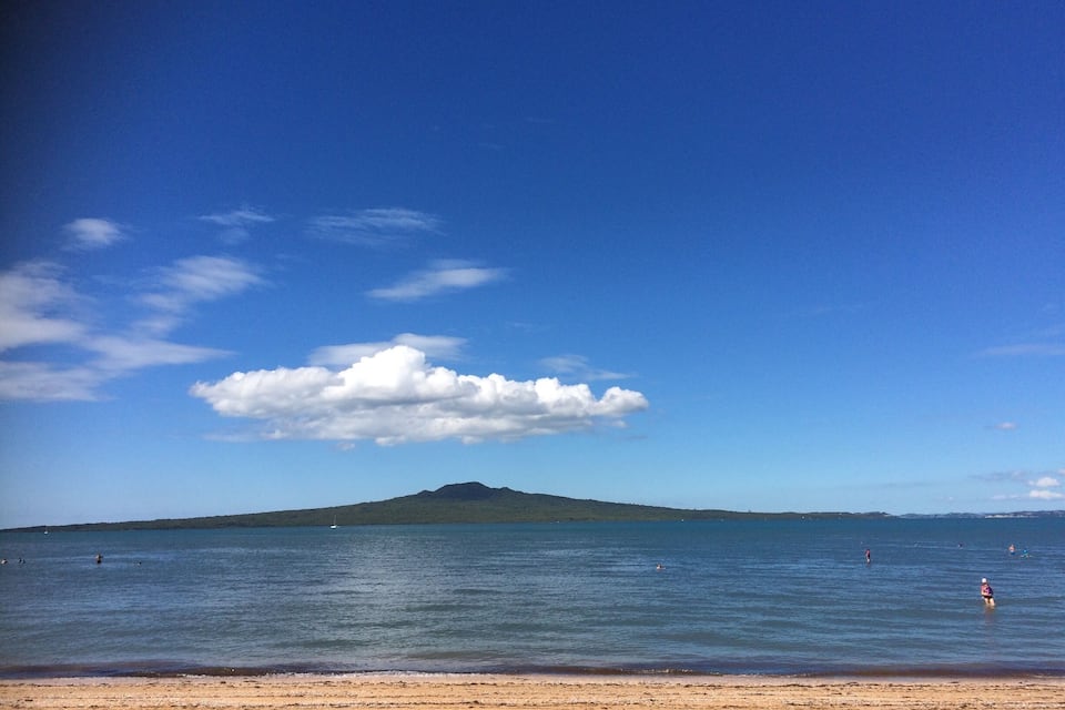 Ein Strand mit blauem Himmel, ruhiger See und einem fernen Berg.