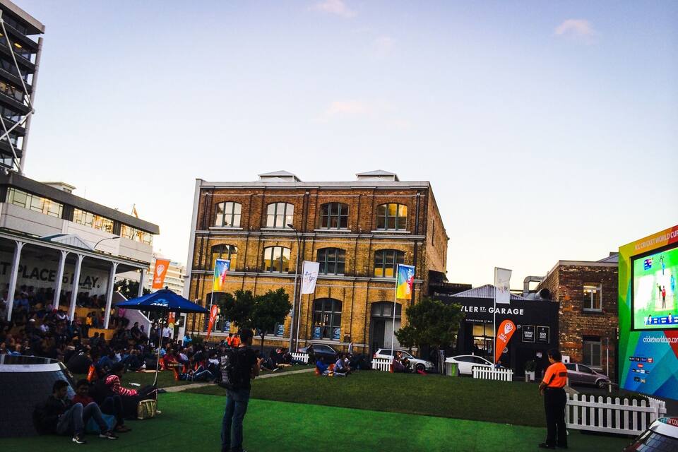 A historic building with large windows and a brick facade, surrounded by a crowd of people and a green lawn.