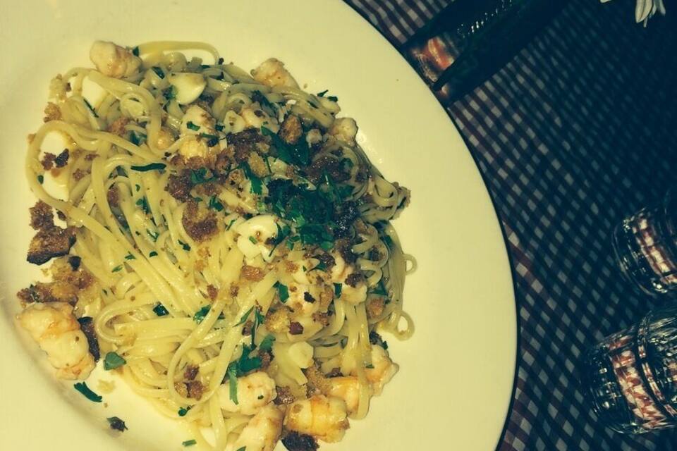 Un plat de pasta amb gambes i herbes sobre una taula amb mantell de taula quadriculat.