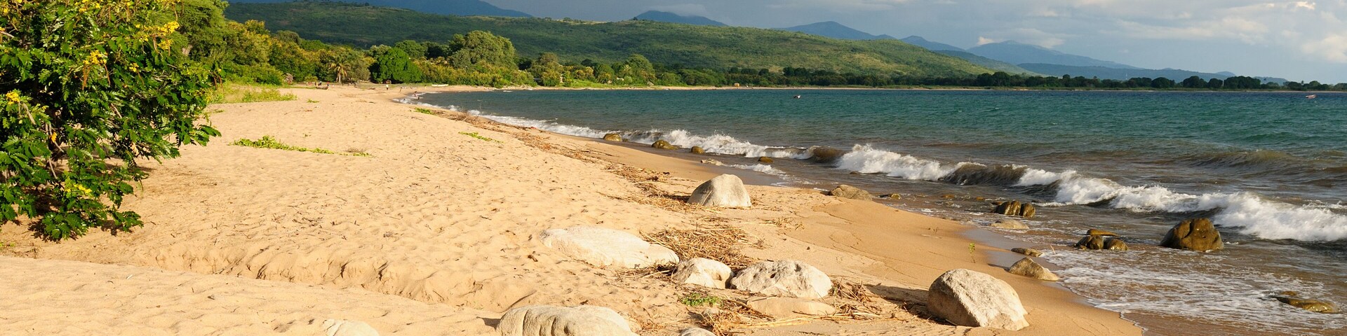 Una playa arenosa con grandes rocas y una vista de colinas verdes al horizonte.