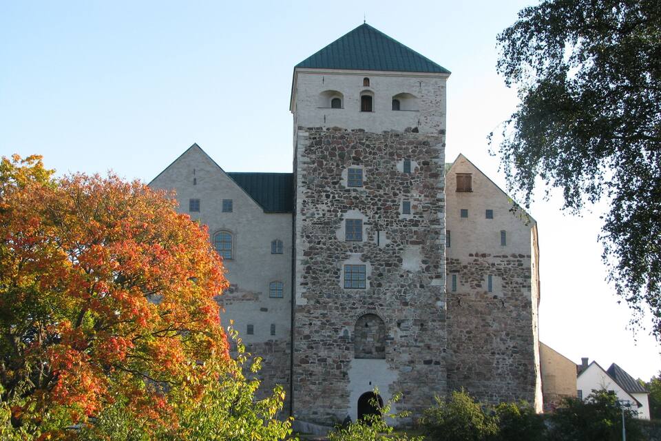Een historisch stenen gebouw met een toren, omgeven door herfstbladeren.