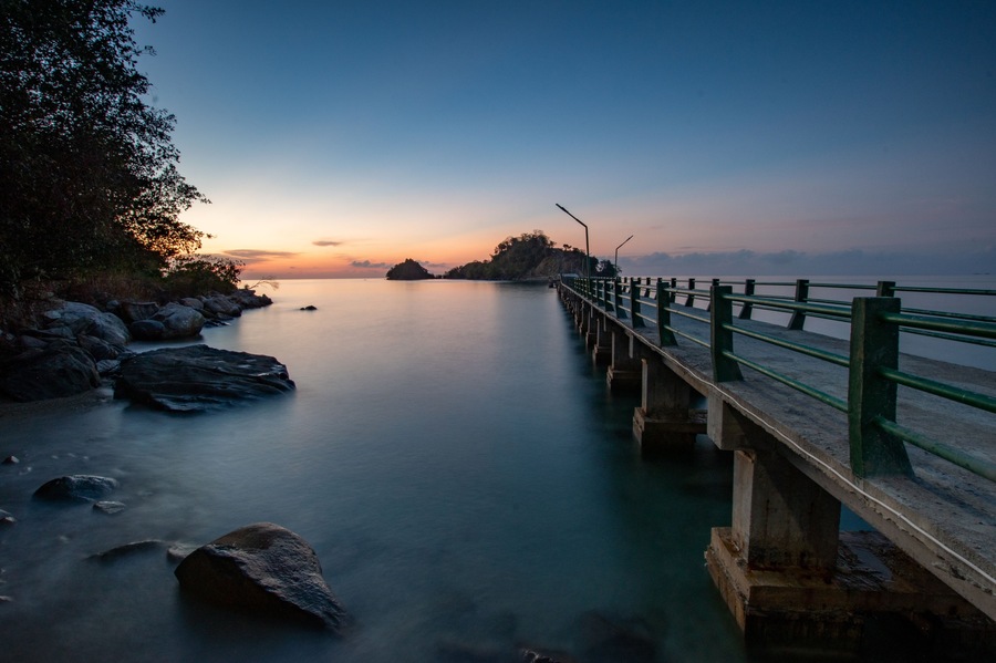 Sunset on a bridge connecting sulawesi main island and sabang tende island, tolitoli, central sulawesi, indonesia with visible rock and coral using long exposure