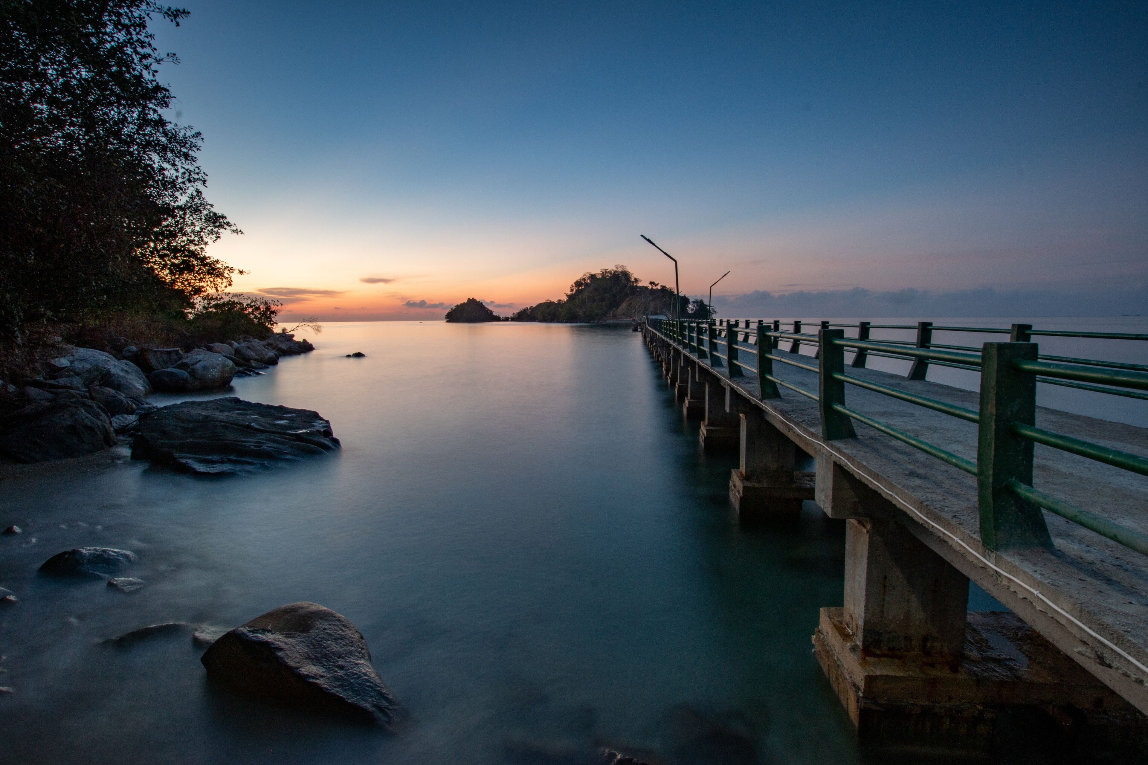 A pier extending into calm water with a sunset in the background.