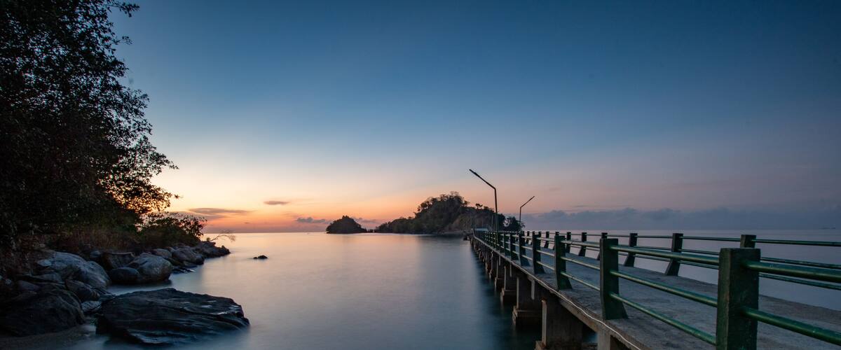 A pier extending into calm water with a sunset in the background.